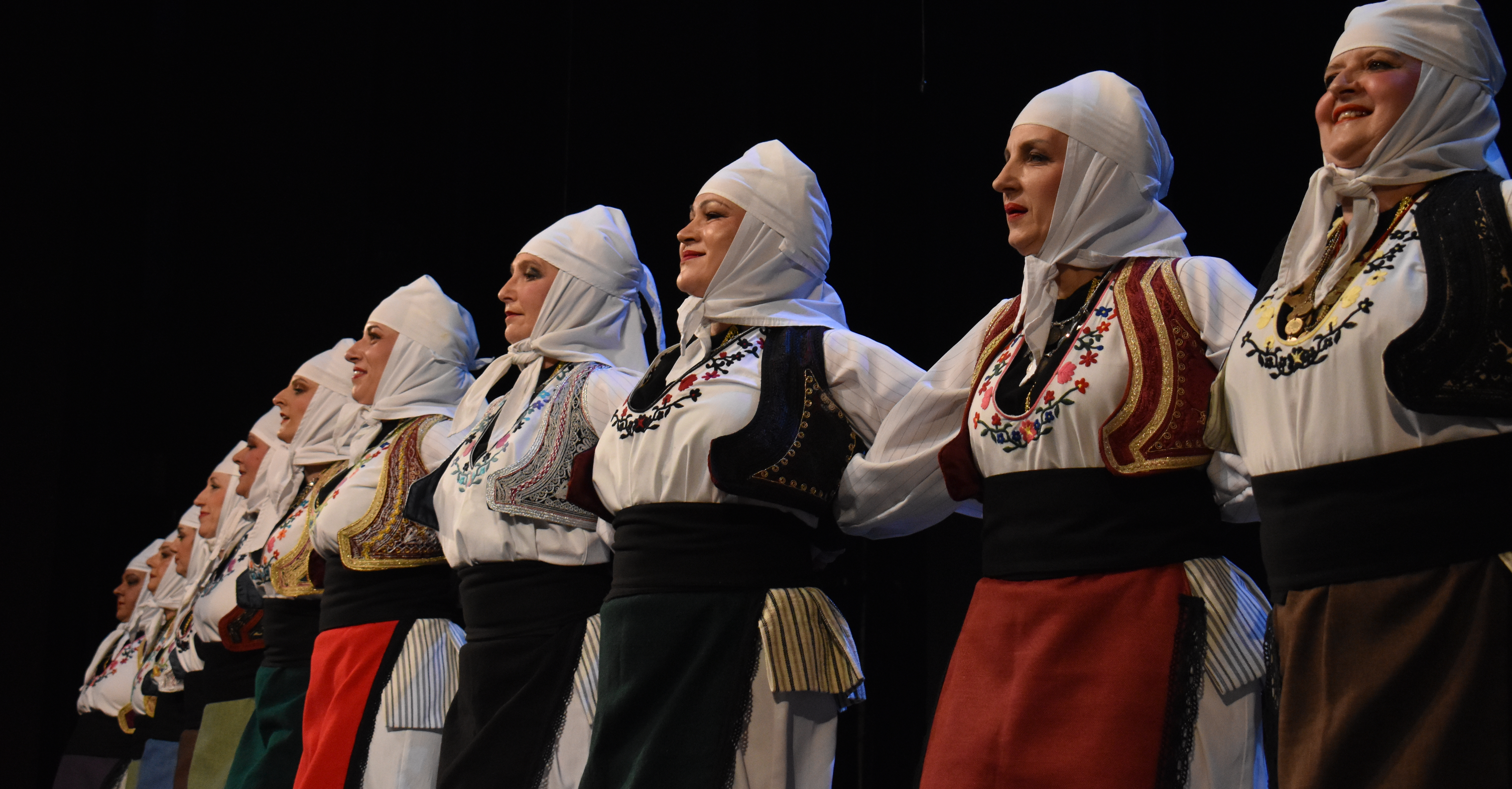 Žene u srpskim narodnim nošnjama sa belim maramama igraju kolo na sceni / Women in Serbian folk costumes with white headscarves dancing kolo on stage